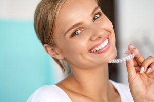 A close up picture of a smiling woman using a teeth whitening tool.